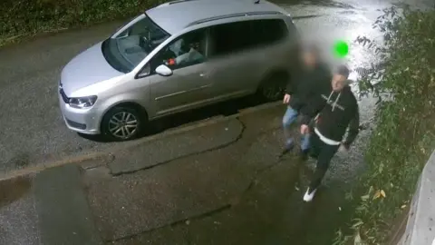 Leicestershire Police A screengrab from CCTV footage which shows two men walking along a pavement. One man, whose face is blurred, wears a dark coat and blue jeans. The other man, Nathan Gothard, is wearing a black hoody with white detail on and dark trousers.
