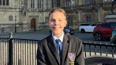 St Edward's School Andrii Rokotianskyi smiles as he stands outside the House of Lords. He wears a school blazer and his long, brown hair is tied back in a bun.