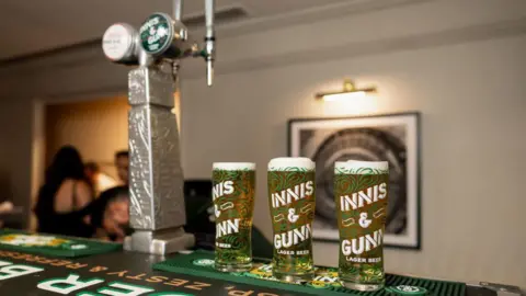 Three pints of Innis and Gunn on a bar with two Innis and Gunn taps next to it.