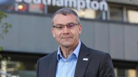 University Hospital Southampton NHS Foundation Trust David French has short grey hair, is wearing a blazer and shirt. He is standing outside of Southampton General Hospital.