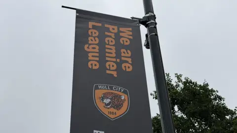 James Hoggarth/BBC Close-up shot of a banner on a lamp-post promoting Hull City. It has the club emblem and reads: "We are Premier League"