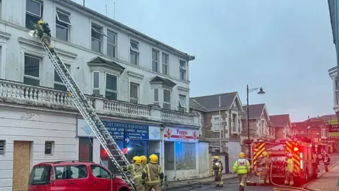 Island Echo A ladder rests against a third floor window of the hotel with a firefighter looking into the window firefighters and a fire engine in the road below