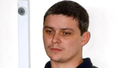 PA Ian Huntley with short dark hair wearing a black collared shirt.