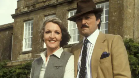 Keith and Bowles in To The Manor Born - posing in character outside their stately home