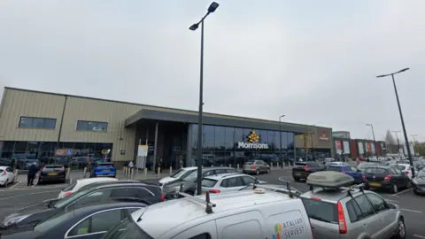 A general view of the Morrisons store in Kirkby, Merseyside. It is a glass-fronted building, including the Morrisons' logo, seen from the car park. 