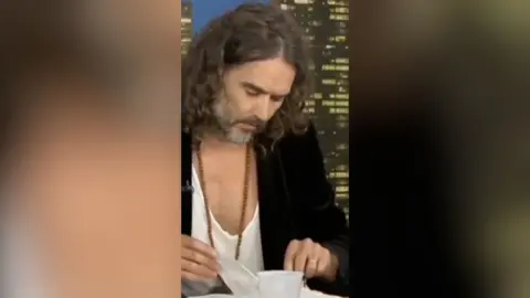 A man with shoulder-length curly hair flips through a Bible