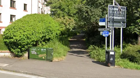 The entrance to the Restalrig Railway Path from Easter Road. A sign reading "Restalrig Railway Path" in white writing on a black background is visible next to greenery.