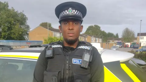 Abdullah Ahmed PC Abdullah Ahmed wears a serious expression as he stands in full uniform next to a police car