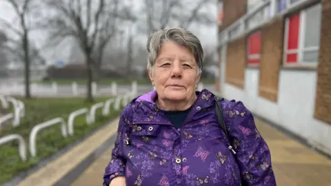 Brenda Morgan walking past the Royal Mail building in Yate wearing a purple coat