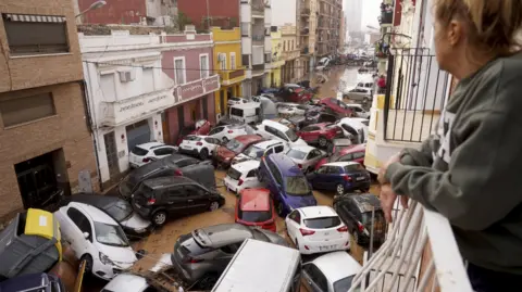 AP A woman looks out from her balcony at a pileup on a flooded street in Valencia on October 30