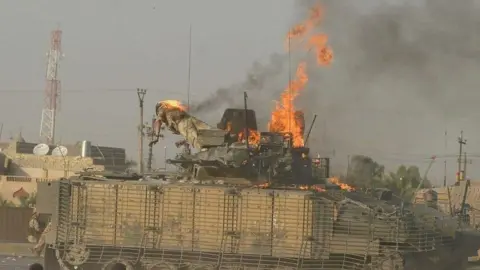 Reuters A military tank has flames coming from the top. A soldier whose clothing is on fire appears to be falling or jumping from the tank.