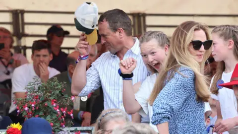 Chris Jackson/Getty Images Peter Phillips takes his cap off as Harriet Sperling stands in a blue dress and sunglasses a little lower down