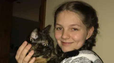 Family handout A head and shoulders shot of Libby Mycroft cradling a black and brown cat. Libby has brown hair tied in plaits and is smiling at the camera.