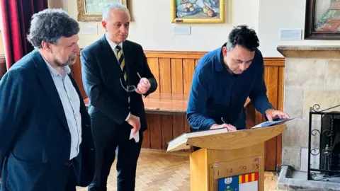 Three men at a lectern signing a document