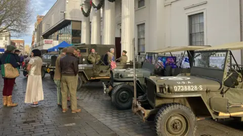 Row of green army jeeps with people standing around it