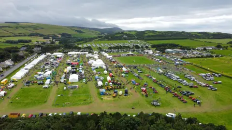 CALLUM STALEY/ CJS PHOTOGRAPHY An aeriel view of large fields with a number of marquees, cars and people scattered around. 