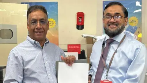 Post Office Chani Gill (left) presented with a framed certificate for his long service at Cobham Post Office