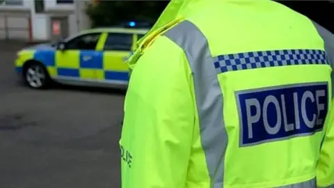 A police officer in a high-vis jacket and a car in the background.