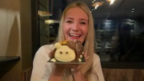 Lily-May Vaughan smiling as she holds a caterpillar birthday cake