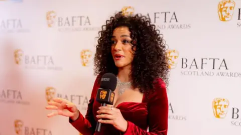 Getty Images Shereen Cutkelvin on the red carpet - she is wearing a red dress and holding a microphone