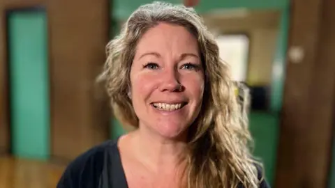 Martin Giles/BBC Katie Fryer-Olliffe, young women’s development worker, is looking directly at the camera and is smiling. She wears a black top and has long blond wavy hair.