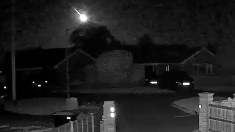 A doorbell camera image at night with a bright meteor flying across the sky.