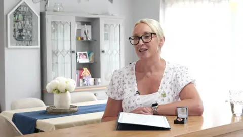 Susan Walker, wearing a white top, talks to the BBC in her kitchen