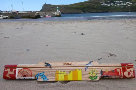 Lesley Sleight The baton sits on a sandy beach. 