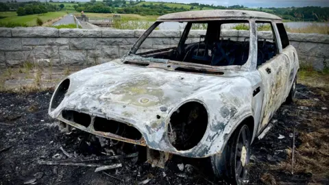 A burnt out car. The ground around the car is also burnt.