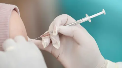 Reuters A needle held by a hand wearing a surgical glove, injecting something into an arm.