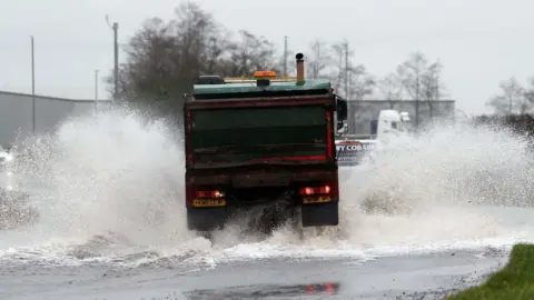 A lorry drives through a flooded road in County Antrim with spray coming up on either side of it