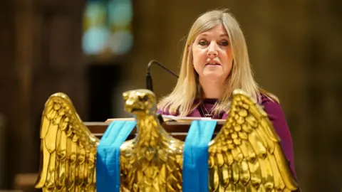 PA Media woman with blonde hair stands behind a gold eagle statue as she reads in churh
