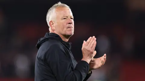 Getty Images Chris Wilder, a man in his fifties, wearing a dark top. He is looking into the far distance and applauding.