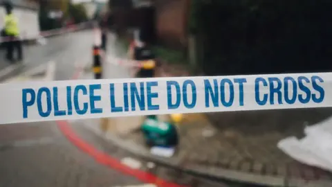 Police tape telling people not to cross as emergency workers attend the scene of an accident or crime