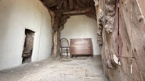 Dr Jenner's House The inside of a small stone building - the walls are rendered white and there is a wooden chair in the corner. On one wall, there is a tiny fireplace.