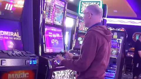 Undercover BBC reporter Greg Clark standing playing video games machines at an Adult Game Centre