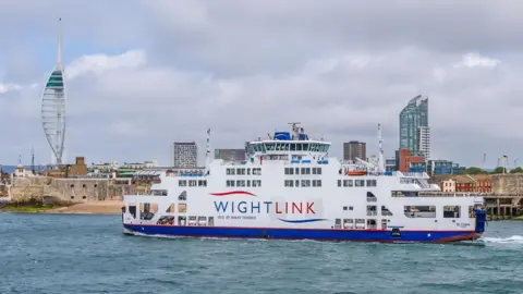 MV St Clare sails into Portsmouth. The white ferry bears red and blue Wightlink livery. In the background is the Spinnaker Tower.