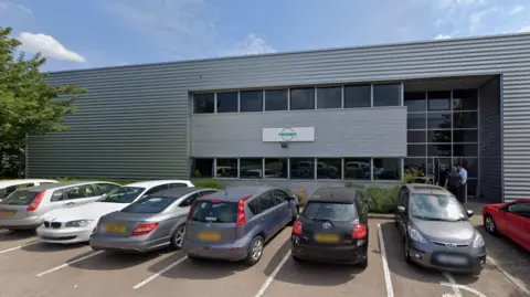 Google A grey distribution warehouse or offices in St Albans, with cars parked outside and some greenery.