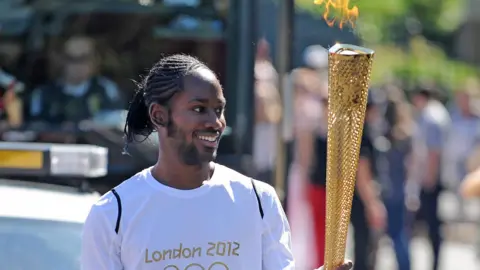 PA Media ason Arday carries the Olympic Flame on the Torch Relay leg between Sutton (London Borough) and Merton (London Borough)