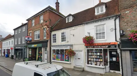 A street view of Kim's Bookshop in South Street, Chichester, which is a white building standing between two brown brick terrace buildings.