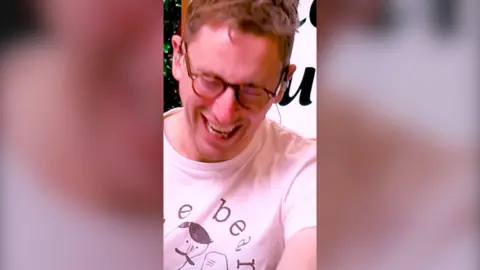 A close up of podcast host and comedian John Robins bent over laughing