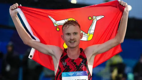 PA Mullarkey holding up the Manx flag behind his head 