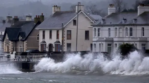 Getty Images A row of houses by the sea. There are large waves hitting the wall between the sea and the houses.