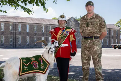 Crown Copyright 2025 Jones in military uniform next to man in red ceremonial military uniform and a military goat.