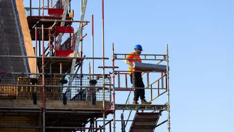 A worker on scaffolding outside a house under construction.