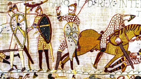 Getty Images Close up of frame of the Bayeux Tapestry, showing intricate embroidery in gold, red and cream hues, and depicting the death scene of Harold at the hands of William the Conqueror during the Battle of Hastings