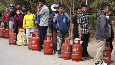 Getty Images Nepali consumers wait in line carrying empty LPG cylinders as they rush to gas depots to refill them