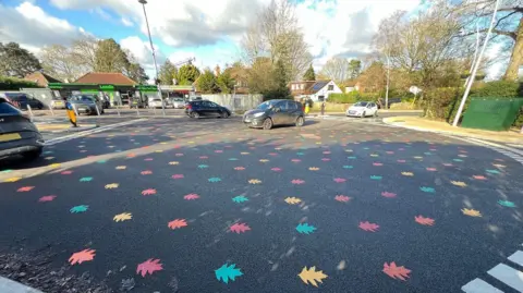 Cars driving across one of the rainbow leaf roundabouts.