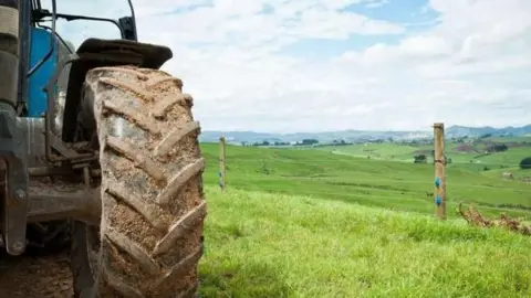 A partial picture of tractor focused on the large back wheel on the right hand side with grassy fields in the background