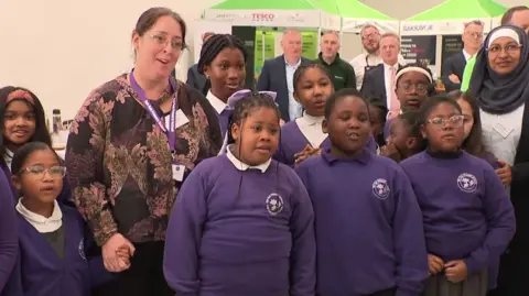 A radical  of schoolchildren successful  purple jumpers singing Happy Birthday to King Charles